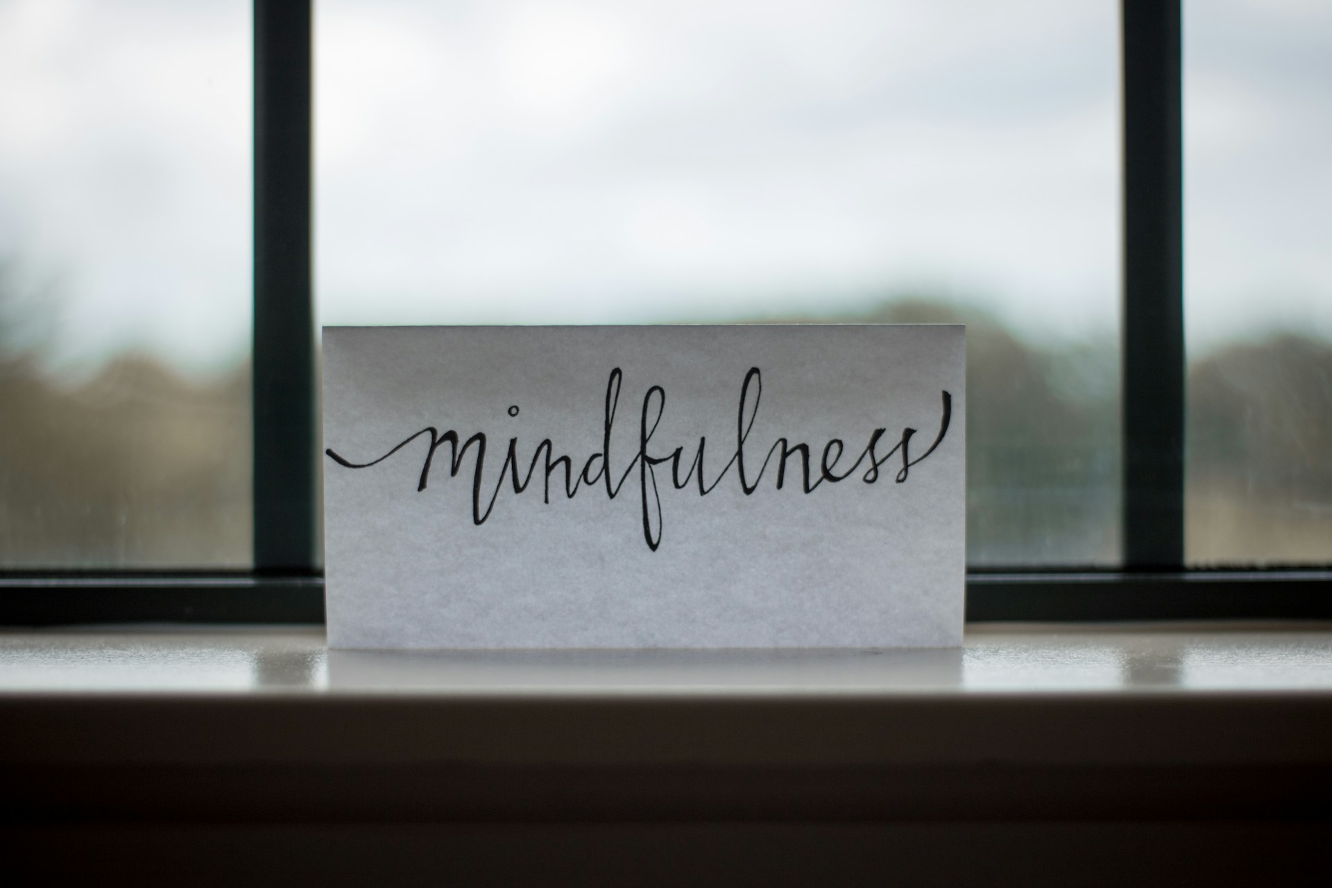 Achtsamkeitsübungen für Zuhause- Schriftzug Mindfulness auf einem Papier vor einem Fenster